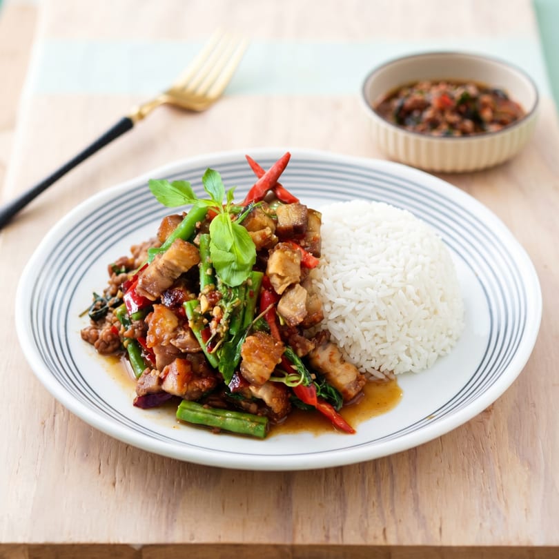 Crispy pork belly stir-fry with basil, green beans, red chilies, and white rice on a plate.
