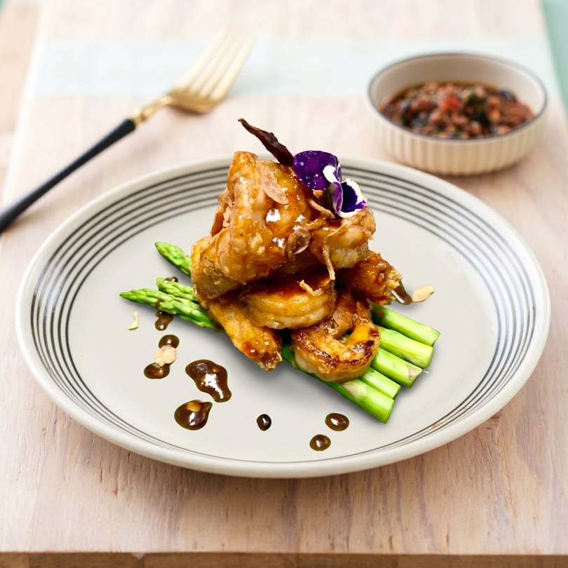 Glazed shrimp and chicken skewers with asparagus, garnished with a purple flower and sauce.